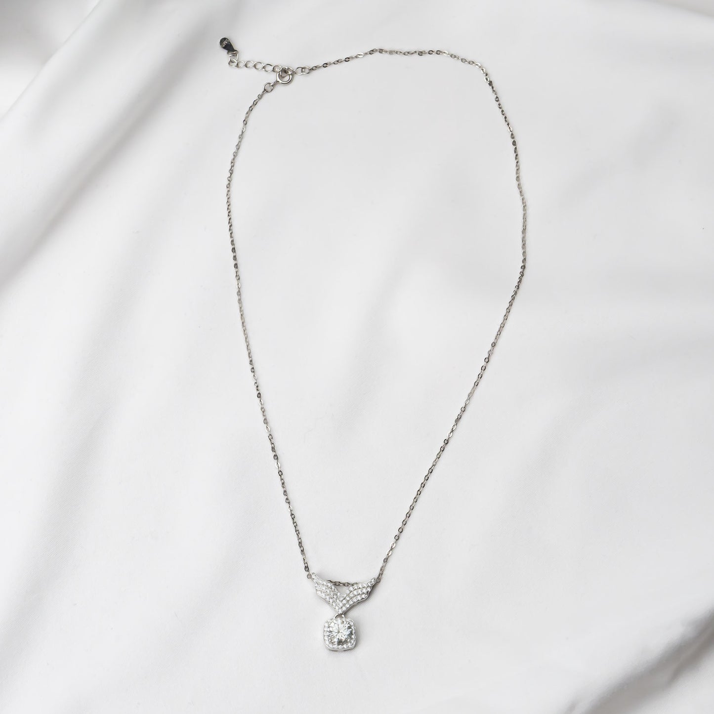 Silver necklace with a mossanite pendant on a light gray background