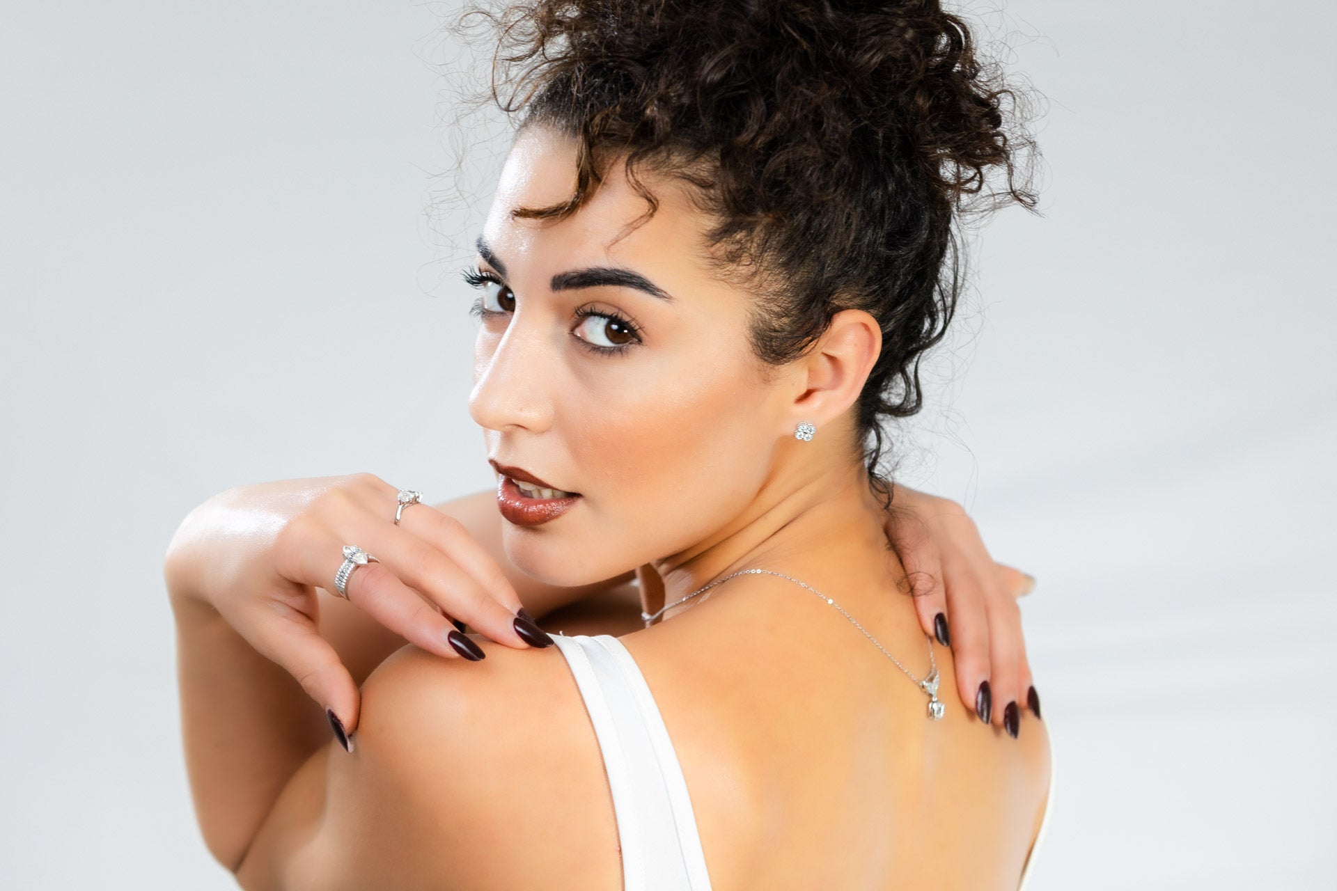 Woman with styled hair and makeup wearing a white top against a light background